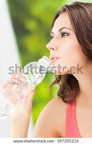 Portrait of young woman drinking water from bottle, outdoors. Focus on bottle.