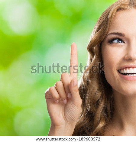 Young happy smiling blond attractive woman, showing one finger or idea gesture, outdoors