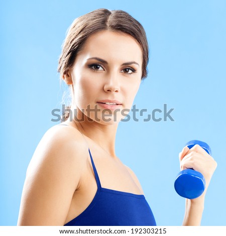 Cheerful woman in fitness wear exercising with dumbbell, over blue background