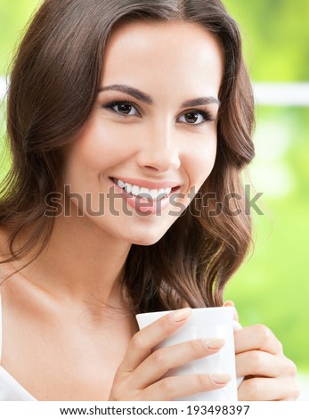 Portrait of young happy smiling woman drinking coffee or tea, at home