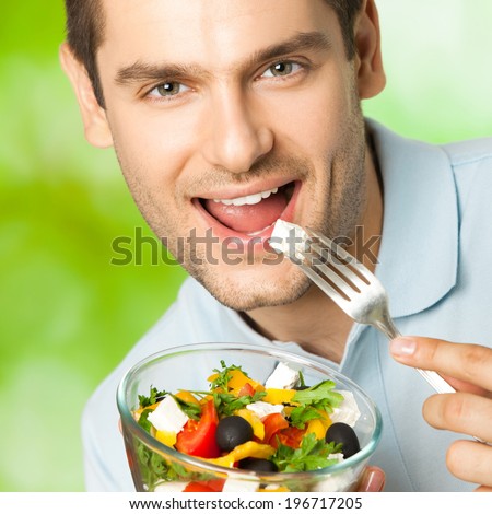 Young smiling man eating salad, outdoors