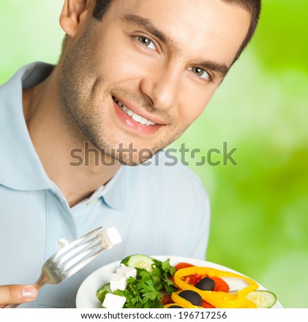 Portrait of young happy man eating salad, outdoors