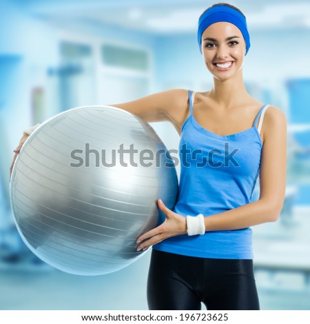 Portrait of young happy smiling woman with fitness ball, at fitness club or center