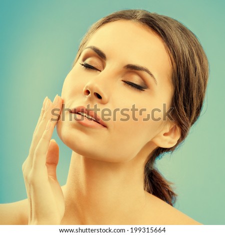 Portrait of beautiful young woman touching skin or applying cream, over blue background