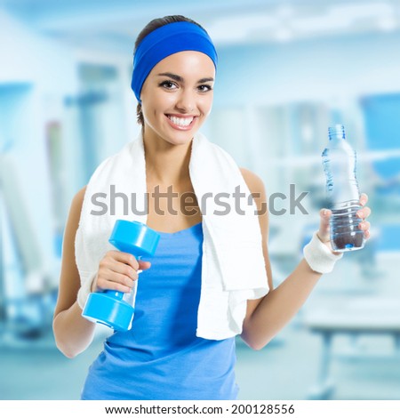 Portrait of happy smiling young woman in fitness wear with bottle of water, at fitness club or center