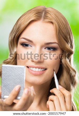 Portrait of young happy smiling woman with make up brush and mirror, outdoors