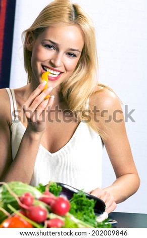 Young attractive smiling woman with pepper and vegetables at kitchen