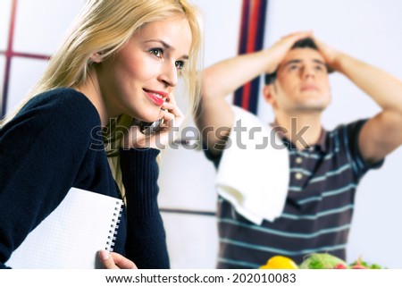 Young happy smiling attractive businesswoman on cellphone and cooking man at kitchen. Focus on woman.