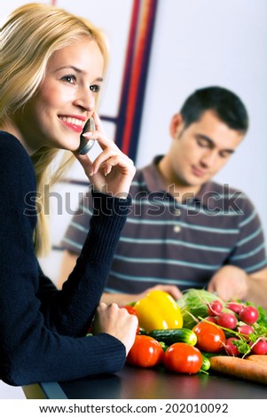 Young happy smiling attractive businesswoman and cooking man at kitchen. Focus on woman.