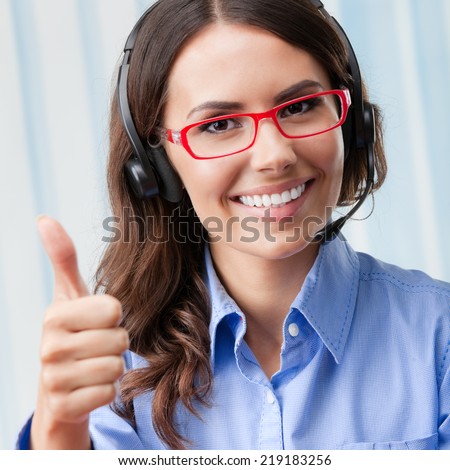 Portrait of happy smiling cheerful young support phone operator in headset, showing thumbs up gesture, at office