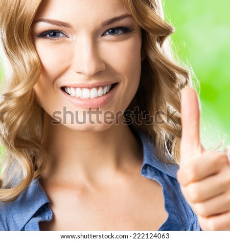 Portrait of beautiful young happy smiling blond woman with thumbs up gesture, outdoors