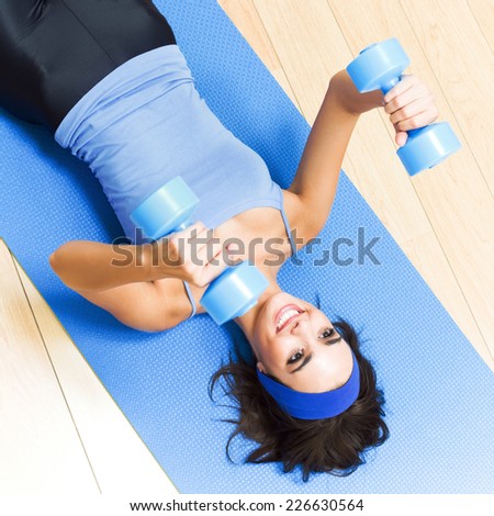 Young happy woman exercising with dumbbells at home
