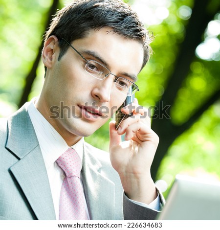 Young happy smiling business man working with laptop and cellphone, outdoors