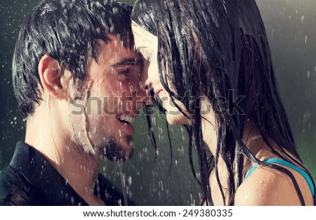 Young amorous couple hugging and kissing under a rain, outdoors