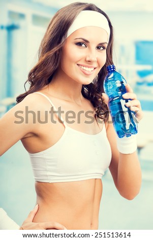 Happy smiling young beautiful woman with bottle of water, at fitness club or gym