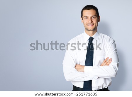 Portrait of cheerful young businessman with crossed arms pose, with blank copyspace area for text or slogan, against grey background