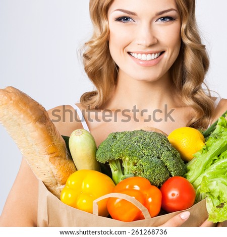 Portrait of happy smiling cheerful woman holding grocery shopping bag with healthy vegetarian raw food, against grey background. Healthy eating and dieting concept.