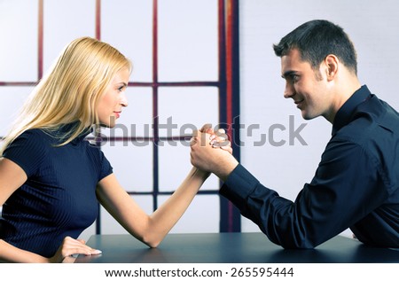 Young happy couple or two businesspeople fighting in arm wrestling, at office