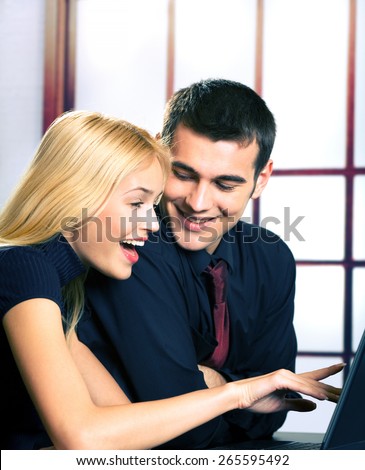 Two cheerful young businesspeople with laptop, working, chatting, playing or searching something at internet