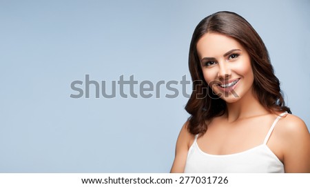 Portrait of beautiful cheerful smiling young woman, on grey, with blank copyspace area for text or slogan