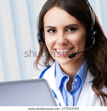 Portrait of happy smiling young doctor in headset, using laptop, with blank copyspace area for slogan or text