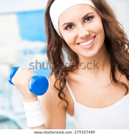 Young happy woman in fitness wear exercising with dumbbell, at fitness center or gym