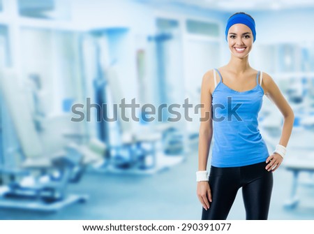 Portrait of young happy smiling woman in blue sportswear, at fitness club or center, with blank copyspace area for slogan or text message. Beauty and health concept.