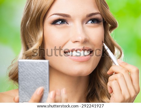 Portrait of young happy smiling lovely woman with make up brush and mirror, outdoors. Visage and cosmetics concept.