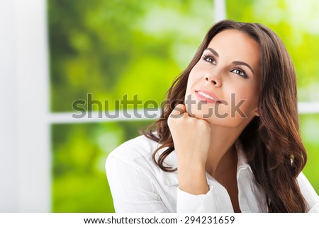 thinking smiling attractive brunette businesswoman looking up, at office, with blank copyspace area for slogan or text