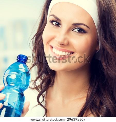 Happy smiling young lovely woman with bottle of water, at fitness club or gym