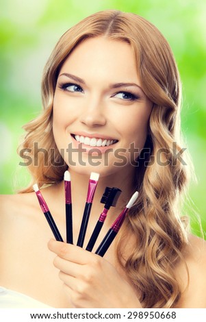 Portrait of young cheerful blond lovely woman with make up tools, outdoors. Beauty, visage and cosmetics concept.