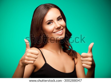 Portrait of beautiful cheerful smiling young woman in black tank top clothing, showing thumb up gesture, on green background