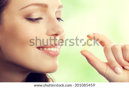 Young smiling lovely brunette woman with Omega 3 fish oil capsule, outdoor