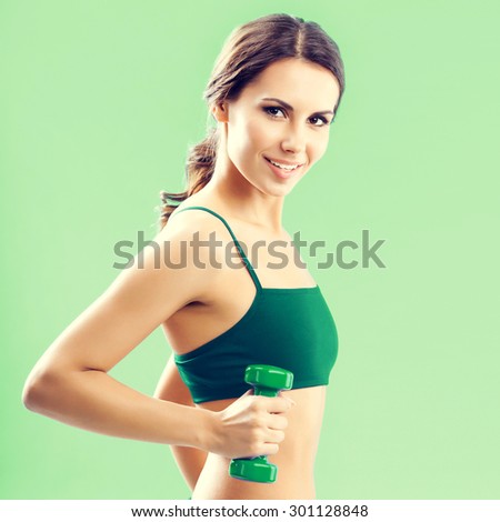Portrait of smiling young lovely woman in fitness wear exercising with dumbbell, over green background