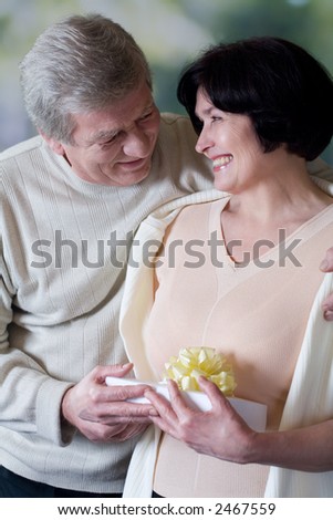 Elderly happy embracing couple with gift box, smiling