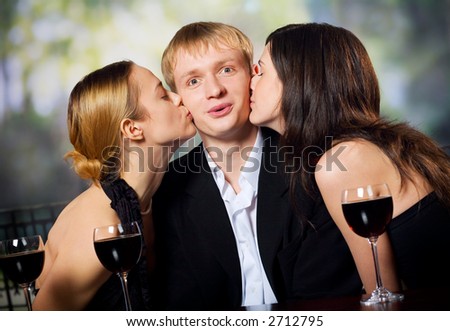 Two young attractive sweet women kissing man with redwine glasses at the celebration or party