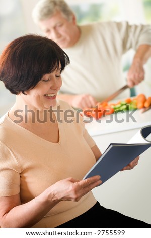 Elderly happy couple cooking at kitchen. Focus on woman.