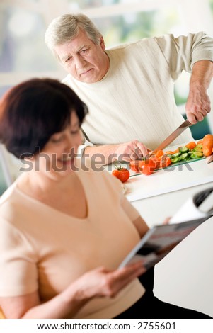 Elderly happy couple cooking at kitchen. Focus on cooking man.