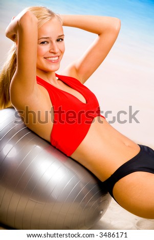 Young attractive happy smiling woman in sportswear with pilates gym ball on sea beach