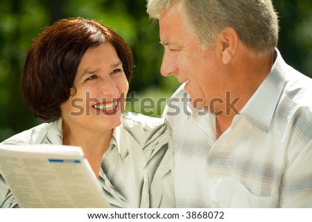 Happy smiling attractive elderly couple reading together outdoors