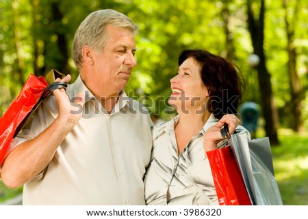 Senior attractive happy smiling couple with shopping bags walking in park, looking at each other