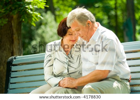 Happy elderly couple listening music in headset or praying together, outdoors