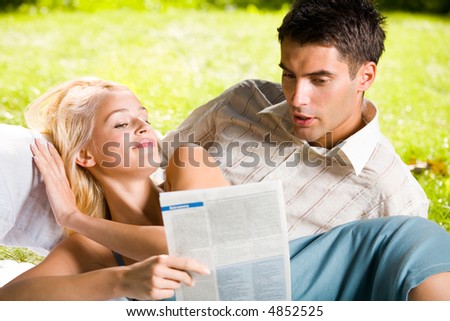 Happy smiling young couple reading together outdoors