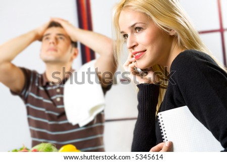 Young happy smiling attractive businesswoman on cellphone and cooking man at kitchen. Focus on woman.
