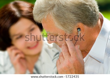 Happy elderly couple listening music in headset together, outdoors. Focus on man.