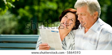 Happy elderly couple reading together outdoors. Focus on woman. To provide maximum quality I have made this image by combination of two photos.