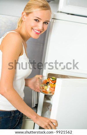 Young happy smiling woman with salad at domestic kitchen