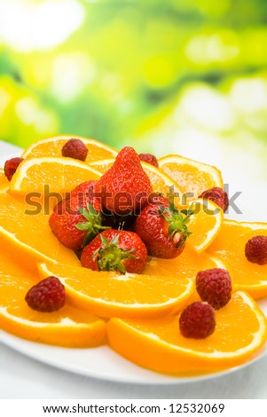 Photo of plate with orange, strawberry and raspberry, outdoors