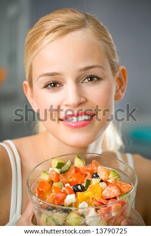 Young happy woman with vegetable greek salad at domestic kitchen