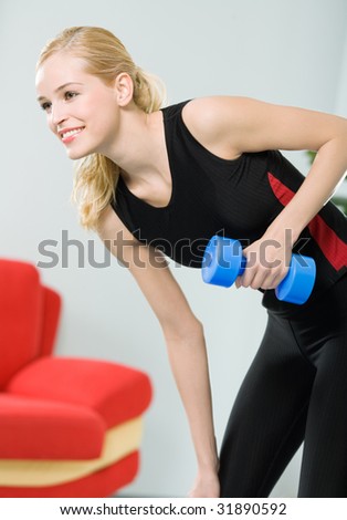 Young happy woman doing exercises with dumbbell at home